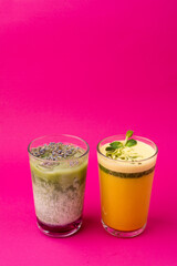 Two glasses of sweet matcha beverages, top view on bright magenta background