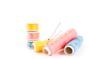 Three spools and bobbins of thread of yellow, blue and pink color with needles on a white background in a minimalistic style with a place for text. Items for needlework, embroidery and sewing.