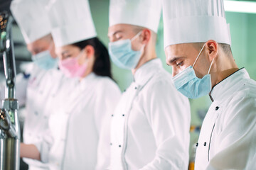 Chefs in protective masks and gloves prepare food in the kitchen of a restaurant or hotel.