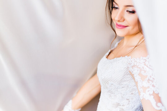 bride in white dress with a beautiful makeup under  white curtai