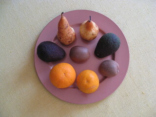 varias frutas: dos peras, dos aguacates, dos kivis, dos naranjas cítricos, carnosas y de agua sobre plato rosa, ecológicas. Vista cenital
