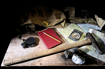 Geological tools - maps, hammer, notepad, geological compass, magnifying glass - on a wooden table