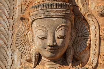 Fototapeta na wymiar Carved portrait of a beautiful smiling woman on a wall of ancient ruined Buddhist temple in Indein, Inle lake area, Myanmar