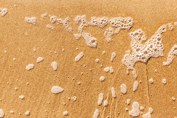 Sand on the beach and light wave with foam. Background with copy space.