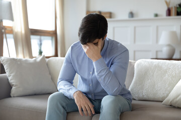 Fototapeta premium Upset young caucasian man sit on sofa in living room feeling depressed distressed with life relationships problems, unhappy sad millennial male suffer from mental or psychological issue, yearn at home