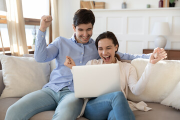 Overjoyed young man and woman relax on sofa in living room triumph winning online lottery on laptop, excited caucasian couple feel euphoric get pleasant good unexpected email on computer