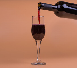 a bottle of red wine and a glass on a beige background