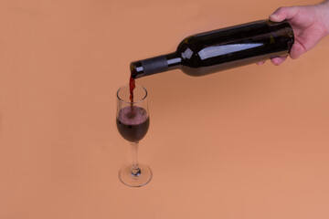 a bottle of red wine and a glass on a beige background