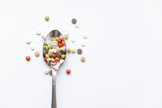 Medicine and health, treatment, pharmaceutics, coronavirus, pandemic, epidemic concept - layout one silver big tablespoon with multi-colored tablets and capsules on a white background copy space.