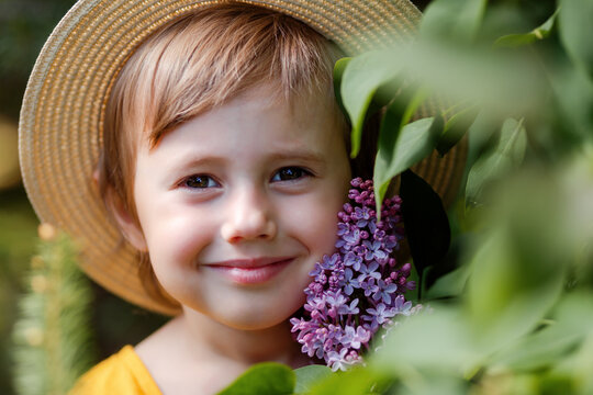 Cute adorble portrait of beautiful little girl in a hat near lilac flowers.