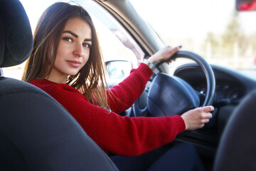Naklejka premium Young beautiful happy woman in red sitting at the wheel new training car.