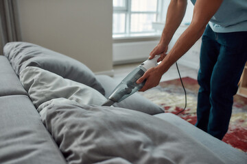 Keeping your home super clean. Cropped photo of a male worker cleaning sofa with handheld vacuum...
