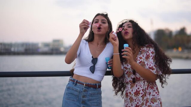 Young hipster women having fun blowing bubbles by the sea