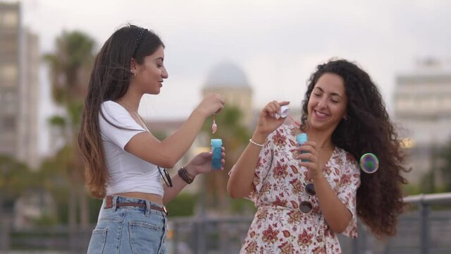 Happy hipster teenage girls blowing bubbles in city, slow motion