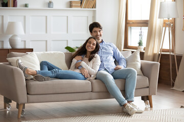 Portrait of smiling young caucasian couple sit relax on comfortable sofa in design renovated living...