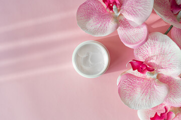 Cosmetic skin face care cream moisturize and orchid flower on pink background. Cosmetology body care lotion