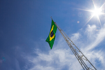 Bandeira do Brasil. 
Bandeira do Brasil hasteada no mastro com o céu azul ao fundo.