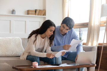 Focused millennial caucasian couple sit on sofa at home manage household paperwork finances...
