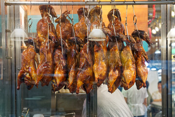 many whole roast duck with heads hanging in a steamy shop window with reflections