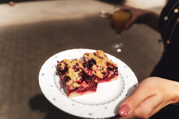 Woman holding plate with two pieces of fruit crumble cake. Outdoor background. Celebration, party, birthday or wedding concept.