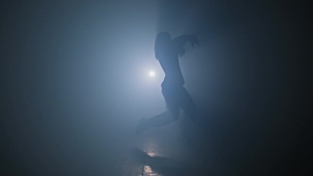 Girl enjoying funky hip hop moves in dark studio with smoke and lighting. Woman dancing on stage in 4K, UHD