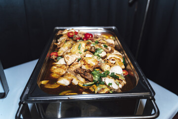 Stainless hotel pan on food warmer with roasted meat pieces and vegetable. Self-service buffet table. Celebration, party, birthday or wedding concept.
