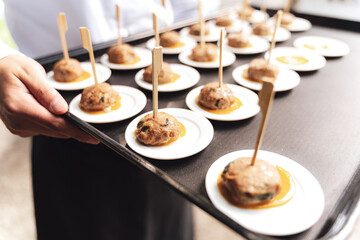 Roasted meatballs served on small white plates. Male hands holding black tray. Selective focus. Celebration, birthday, party, wedding concept.