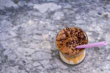 Top view of iced dalgona coffee with chocolate chips and pink straw on marble background,Korean iced coffee. Copy space for text