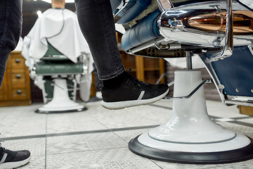 Cropped photo of adjustable barber chair. Barber adjusting barber chair while working in the modern...