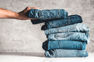 Hands, put the stack of blue jeans on gray background.