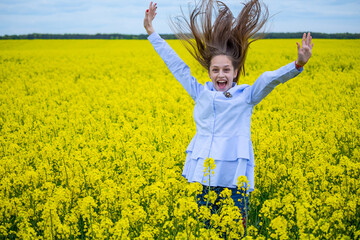 One caucasian beautiful girl with long brown hair is jumping. Happy  smile on female face. Yellow background of blossomed rapeseed. Rural landscape.