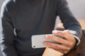 joven utilizando su celular de manera horizontal con su mano izquierda.