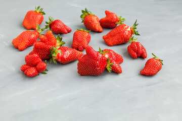 Ugly fruits. Abnormal strawberry shape. Ripe berries on a gray background. Selective focus, copy space