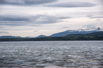 Lake with a layer of ice on top of the water when the lake is thawing from a long winter. Snow capped mountains in background. 