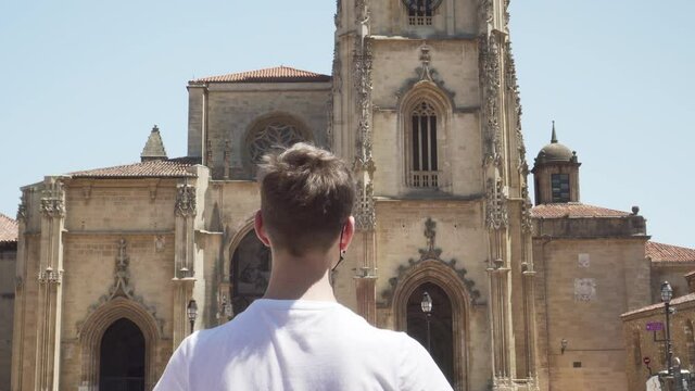 tourist in a medical protective black mask inspects ancient European sights. Oviedo, Spain. The concept of tourism development after the coronavirus pandemic. The view from the back.