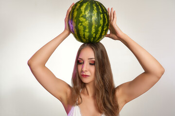 Beautiful girl with big whole watermelon on her had, isolated on studio background. Cosmetics, food, beauty fashion concept, space for text