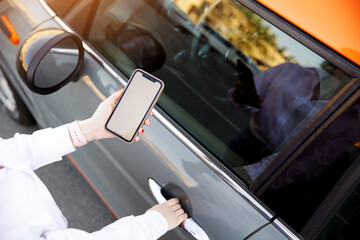 Close up woman hands using mobile phone, communication or online application, standing near car, opening door on city street or parking, outdoors. Car sharing, rental service or taxi app.