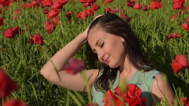 a beautiful girl in a short turquoise dress in a poppy field, among beautiful scarlet flowers, smiles and poses in the wind