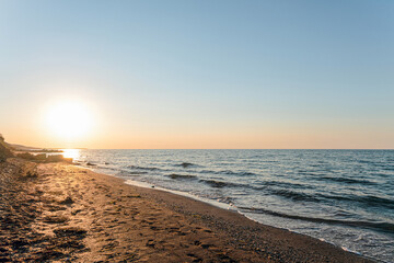 Empty sandy sea beach at sunset. Evening sea landscape with low sun on horizon. Krasnodar region, Russia.