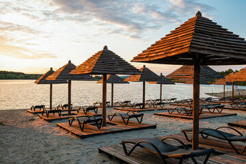 Empty rows resting places on evening sandy beach with brown wooden loungers and umbrellas. Empty sandy beach and rows resting places in the failed tourist season.