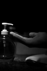 Fotografía en blanco y negro de una mano recibiendo jabón líquido en el cuarto de baño oscuro.