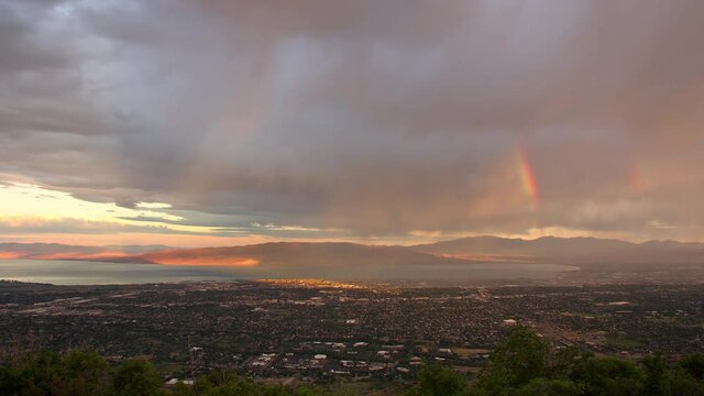 Sunrise stormy time lapse as rainbow forms over city in Utah and sunlight shines on Orem.