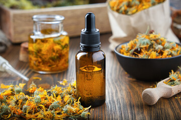 Dropper bottle of calendula essential oil or serum, bowl of dry marigold flowers, jar of calendula...