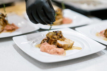 Baked meat with rosemary and sauce. People making meal together awaiting guests. Concept of home cooking healthy food. A cook in gloves decorates meat with rosemary.