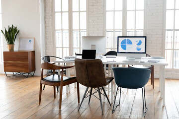 Empty loft office, white wooden table with modern monitors and stylish chairs. Computer screen with market research statistics graphs, professional financial analysts workplace without employees.
