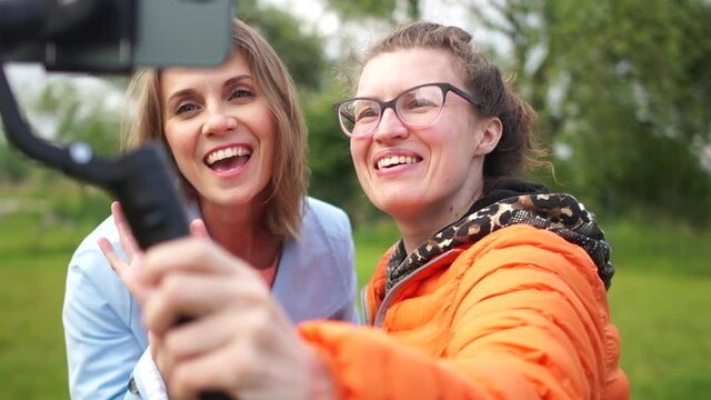 Two person young girl video maker. Two young women blogger posing in front of a smartphone camera. Women shoot video for vlog using smartphone and stabilizer