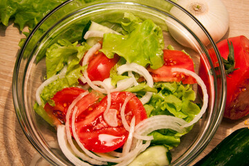Vegetables salad in a glass bowl and vegetables lying on a wooden table