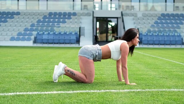 Sexy woman doing exercises on the football field. Corrects hair