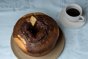 HOMEMADE RUSTIC CAKE, ON THE TABLE HAVING A CUP OF COFFEE IN THE BACKGROUND