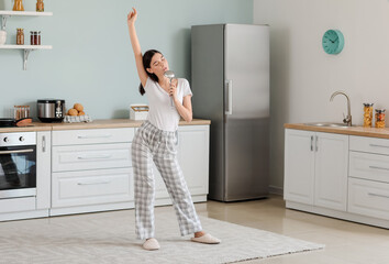 Beautiful young woman dancing and singing in kitchen
